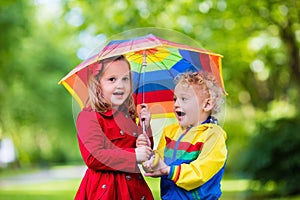 Kids playing in the rain under colorful umbrella