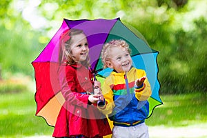 Kids playing in the rain under colorful umbrella