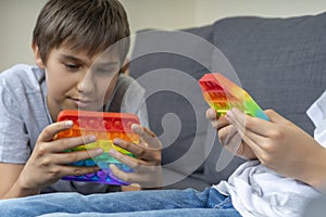 Kids playing with rainbow pop-it fidget toys at home. Push pop it fidgeting game helps relieve stress, anxiety, provide