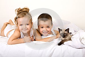 Kids playing with their kitten on the bed