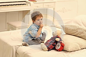 Kids playing with toys. Child in bedroom with silence gesture. Kid put plush bear near pillows and alarm clock, luxury