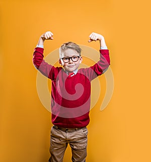 Kids power. Child showing bicep muscles against yellow background. Strong man concept. Stylish pupil of business school