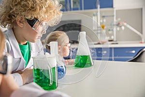 Kids in protective glasses and lab coats making experiment