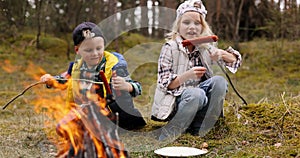 kids put sausages on skewers for roasting over a campfire in forest. camping with kids