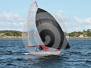 Kids racing a small sailboat with a Black spinnaker at a Junior yachting regatta on a coastal lake