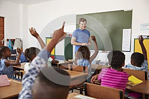 Kids raising hands to teacher in an elementary school class