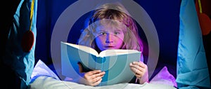 Kids reading a book in the dark home. Child boy reading a book lying on the bed. Dreaming child read bedtime stories