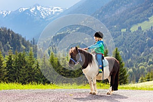 Kids riding pony. Child on horse in Alps mountains