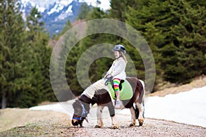 Kids riding pony. Child on horse in Alps mountains