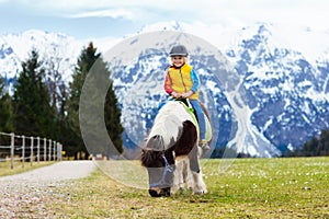 Kids riding pony. Child on horse in Alps mountains