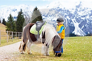 Kids riding pony. Child on horse in Alps mountains