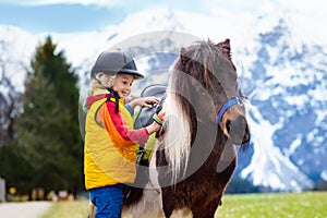 Kids riding pony. Child on horse in Alps mountains