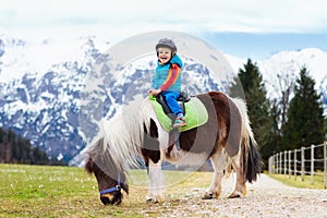 Kids riding pony. Child on horse in Alps mountains