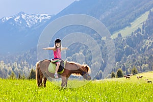 Kids riding pony. Child on horse in Alps mountains