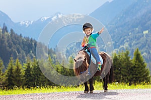 Kids riding pony. Child on horse in Alps mountains