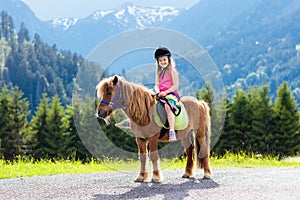 Kids riding pony. Child on horse in Alps mountains