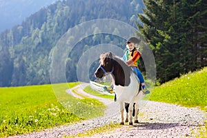 Kids riding pony. Child on horse in Alps mountains