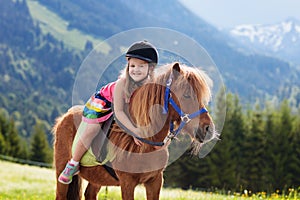 Kids riding pony. Child on horse in Alps mountains