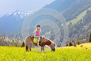 Kids riding pony. Child on horse in Alps mountains