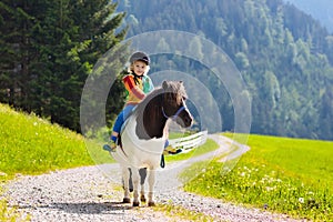 Kids riding pony. Child on horse in Alps mountains