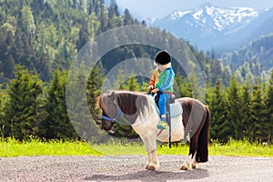 Kids riding pony. Child on horse in Alps mountains