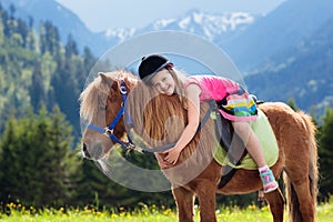 Kids riding pony. Child on horse in Alps mountains