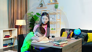 In the kids room sad little boy laying on the table waiting his sister to came to do the homework together happy they