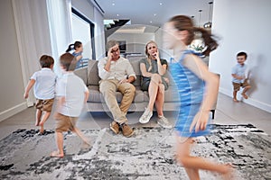 Kids running, mother and father on sofa tired and chaos in living room. Frustrated parents burnout, happy children and