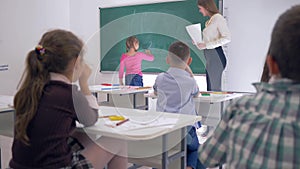 Kids in school, children raise their hands to answer teachers question, schoolgirl goes to blackboard to write simple