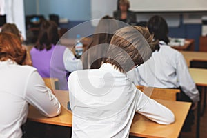 Kids in school writing and taking notes, teens pupils behind desks during the lesson listen to teacher lecture, classroom with