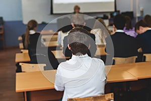 Kids in school writing and taking notes, teens pupils behind desks during the lesson listen to teacher lecture, classroom with