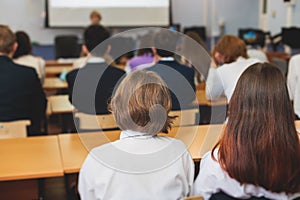 Kids in school writing and taking notes, teens pupils behind desks during the lesson listen to teacher lecture, classroom with