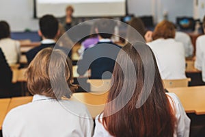 Kids in school writing and taking notes, teens pupils behind desks during the lesson listen to teacher lecture, classroom with