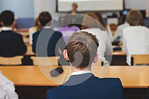 Kids in school writing and taking notes, teens pupils behind desks during the lesson listen to teacher lecture, classroom with