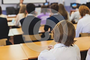 Kids in school writing and taking notes, teens pupils behind desks during the lesson listen to teacher lecture, classroom with