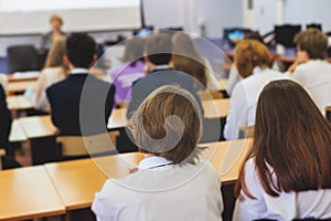 Kids in school writing and taking notes, teens pupils behind desks during the lesson listen to teacher lecture, classroom with