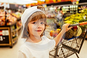 Kids shopping. Joyful beautiful child boy in supermarket buys vegetables. Healthy food for kids.