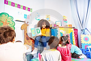 Kids sit around teacher and learn alphabet