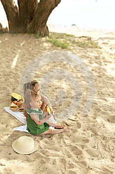 Kids sit on blanket on the shore of a lake on a summer day and eat watermelon
