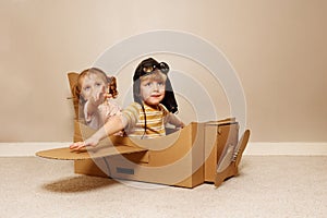 Kids sit in cardboard plane, wear hats and glasses pretend fly