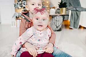 Kids sit on floor near Christmas tree. Happy New Year and Merry Christmas. Christmas decorated interior. The concept of family