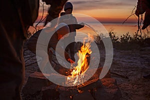 Kids sit near fire on autumn seashore after sunset, warm their hands, have fun together, outside