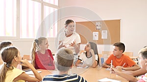 Kids sitting around desk in classroom and studying during lesson. Teacher explaining subject to pupils.