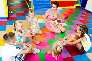 Kids sitting around teacher with small guitar