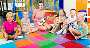 Kids sitting around teacher with small guitar