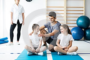 Kids sitting on blue mats with their professional physical education trainer