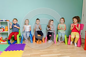 Kids are sitting on the colorful chairs, clapping hand