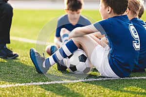 Kids Sitting on Grass Soccer Pitch. Boys in Blue Football Jersey Shirts. Happy Kids on Football Training Camp