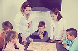 Kids sitting at table with board game and dice at class