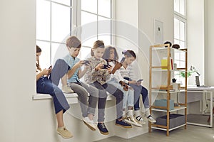 Kids sitting on windowsill, playing games on mobile phones and ignoring each other